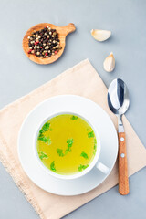 Homemade chicken broth in  white cup garnished with chopped parsley, vertical, top view