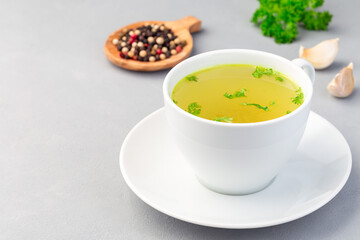 Chicken broth in white cup garnished with chopped parsley, horizontal, copy space