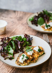 Zucchini fritters with green salad, yogurt on white plate on wooden table