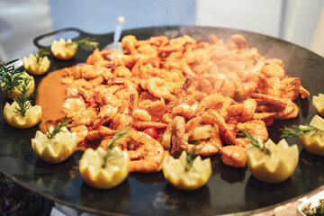 Closeup of shrimps with sauce on big black pan decorated with lemon flower garnish. Celebration, party, birthday or wedding concept.