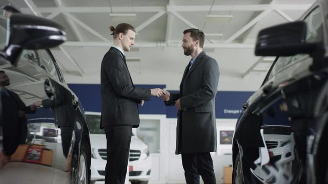 Auto seller gives key to buyer, they shking hands and looks into the camera. Dealer and customer are shaking hands.
