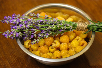 Yellow raspberries in a metal bowl and a bouquet of lavender, a cute romantic still life in summer. High quality photo