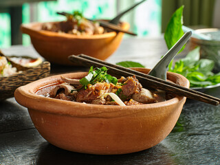 thai bowl of beef noodle soup in clay pot with duck liver