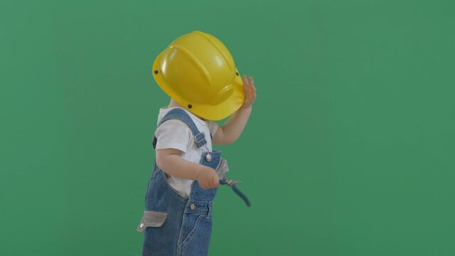Funny child with constructor hard cap on face, baby take off protection helmet and play with dangerous pliers