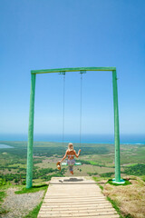 Woman swinging on swings over the green mountains with ocean sea caribbean tropical landscape and horizon line with blue sky. Montana Redonda, Dominican republic. Freedom concept. Touristic place    