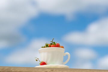 A cup of Strawberries. Strawberries in a white cup on a background of blue sky with clouds. Concept, Good summer morning 