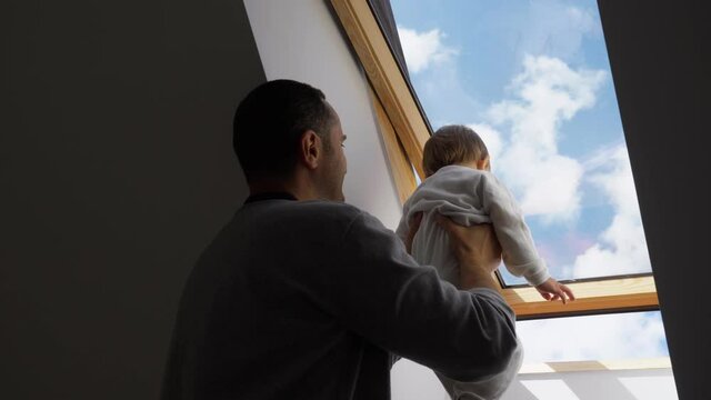 Father lift up baby child to look outside the attic window to blue sky and white cloud, bore of self isolation