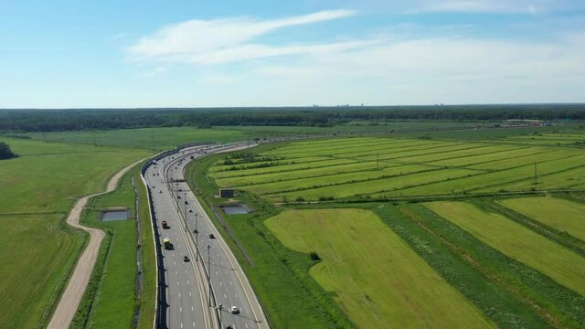 Asphalt ringroad. Speedway with cars through green field near forest. Aerial view from copter