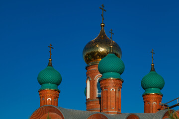Fototapeta na wymiar Golden and green domes of the Orthodox Church against the blue sky