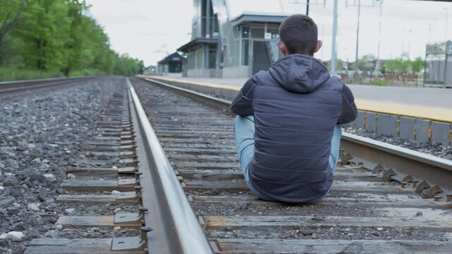 High quality 4k video of a young man sitting on a railway station and looking to the horizont. Depressed person sitting on a railway.