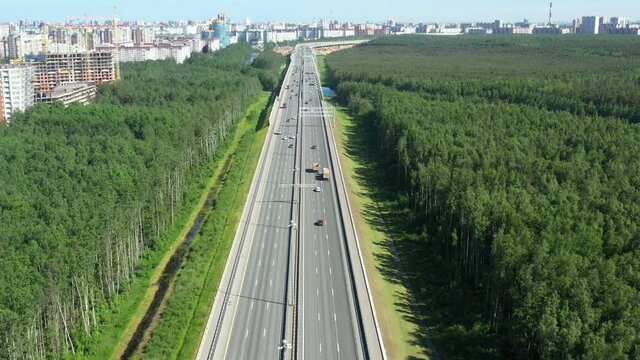 Asphalt ringroad around big city. Speedway through field near forest. Aerial view from copter