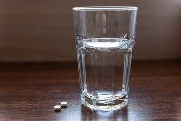 pills lying next to a glass of water on a wooden table