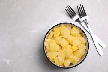 Tasty canned pineapple pieces and forks on light grey marble table, flat lay. Space for text