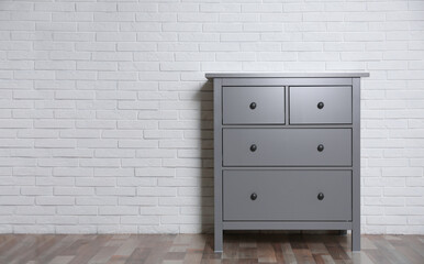 Grey chest of drawers near white brick wall indoors. Space for text