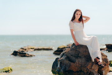 Fototapeta na wymiar Woman with Long Dress Sitting on Rocks By the Sea