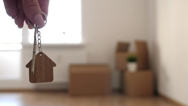 Key with house keychain in hand on background with packed household boxes for movement. Real estate concept