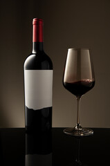 A bottle and a glass of red wine with swirl and waves inside the glass on a beige background