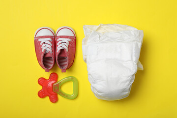 Diaper, child's shoes and teether on yellow background, flat lay