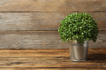 Artificial plant in metal flower pot on wooden table. Space for text