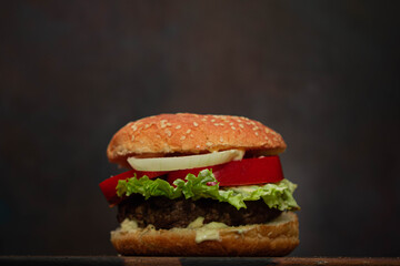primer plano de hamburguesa con lechuga tomate cebolla carne picada sobre madera con fondo oscuro