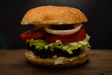 primer plano de hamburguesa con lechuga tomate cebolla carne picada sobre madera con fondo oscuro