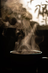 primero plano de taza de te negra con vapor caliente y fondo natural oscuro