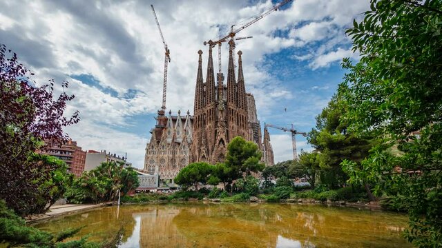 Timelapse view of architectural landmark Sagrada Familia Basilica, a large Roman Catholic church in Barcelona, Catalonia, Spain. Beautiful summer day, spires and cranes against blue sky.