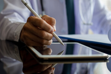 Male doctor work on tablet and writing note in clipboard.