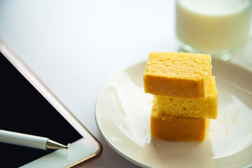 Close up a butter cake pack in a white plate next to a tablet device with a cup of milk background in the morning
