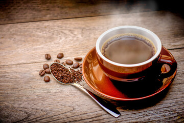 Red cup of coffee with beans on wood table background.