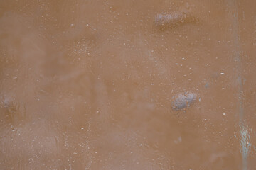 Fototapeta premium A fragment of a glass surface covered with a thin layer of melting ice is located on the background of the color of coffee with milk. Soft focus.
