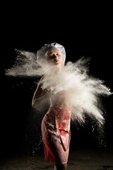 Sensual female baker in red apron with blast of dust