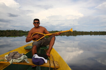 Shirtless man playing the paddle on a boat in Amazon jungle river, Brazil © CYSUN