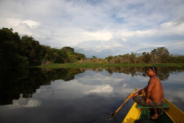 Shirtless man with paddle sitting on a fishing boat at sunset in Amazon jungle river, Brazil © CYSUN