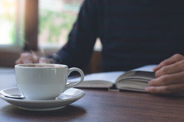 Man reading book with cup of coffee on table at home