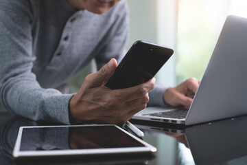Casual business man using mobile smartphone online working on laptop computer from home office