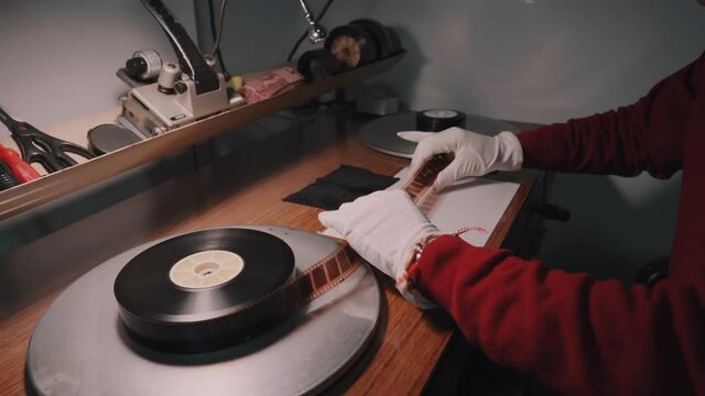A man with white gloves working at a film studio examines a film on special analog equipment. Checks the quality of the film strip
