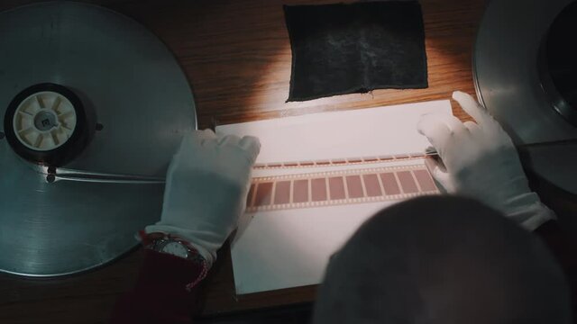 A man working at a film studio, works with old film strip. The camera is above the person and his workplace