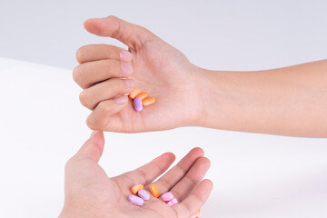 Two hands of patient grabbing medicine pills over white background.
