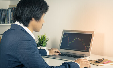 Young Asian Forex Trader or Investor or Businessman in Suit Trading and Looking Forex Charts or Stock Charts in Laptop Monitor in Trader Room in Vintage Tone