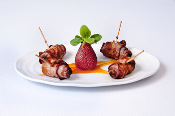 A plate of dates and bacon with strawberry on a white background.