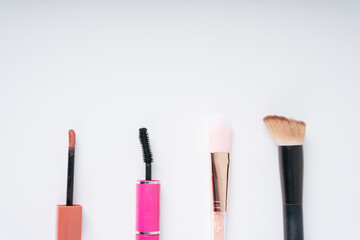 Makeup products on white background. Top view with copy space. Cosmetic set with mascara foundation lipgloss liptint blush-on shader brush.