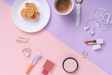 Top view - Cosmetic make up tools and dessert roll over pink and purple background.