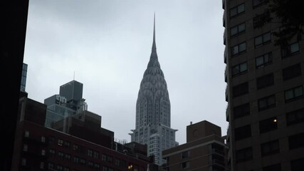 View of Chrysler building between buildings in New York during cloudy day