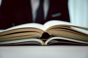 Thick book opened on desk in bookshop, a man in the background.