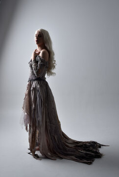 Full Length Portrait Of Girl Wearing Old Torn Wedding Dress. Standing Pose With Rim Lighting On A Grey Studio Background.