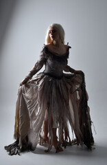 full length portrait of girl wearing old torn wedding dress. standing pose with rim lighting on a grey studio background.