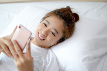 Portrait of an Asian woman lying on a telephone in a bed. She feels relaxed.