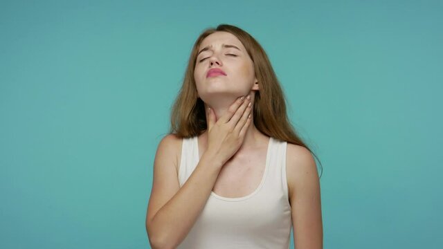 Girl suffering from sore throat, breathing hard rubbing neck, respiratory infection with larynx inflammation, flu symptoms, tonsillitis or thyroid disorders. studio shot isolated on blue background