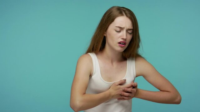 Unhealthy girl clutching chest, feeling acute pain and scared of heart attack, infarction or breast cancer symptoms, healthcare and medical concept. indoor studio shot isolated on blue background